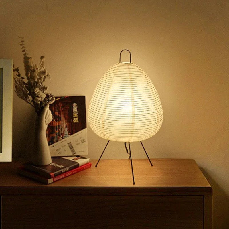 Modern paper lantern table lamp with tripod legs on wooden nightstand in cozy home decor setting