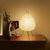 Modern paper lantern table lamp with tripod legs on wooden nightstand in cozy home decor setting
