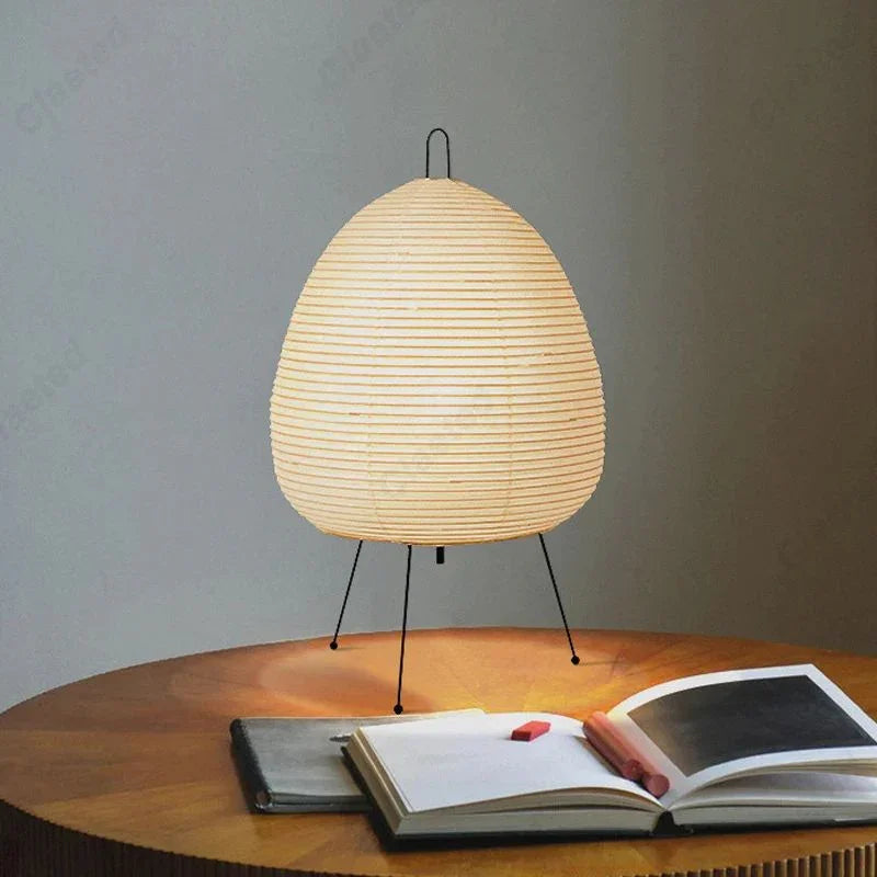 Modern paper lantern table lamp on wooden desk with open book and pencils, minimalist decor