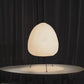 Modern paper lantern table lamp with tripod legs on white round table, dark curtain backdrop